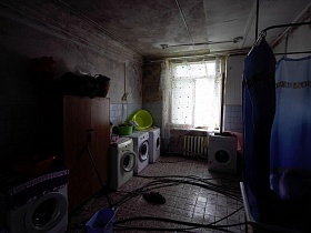 индивидуальные стиральные машинкии ванна с синей шторкой в постирочной коммунального общежития