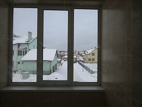 вид на цветные двухэтажные соседние дома через большое окно без гардин