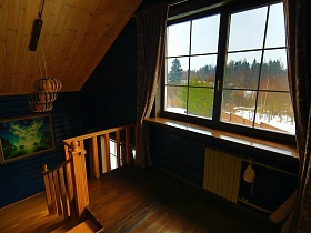 картина на синей стене мансарды с коричневыми шторами на большом окне деревянного загородного дома