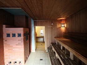 кирпичная печь в парной с трехярусными деревянными полками и открытой дверью в душевую комнату дома из сруба