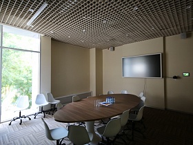 прозрачные стаканы и бутылочки с водой на поверхности коричневого овального стола с белыми стульями, белым телевизором на стене переговорной комнаты в деревне с панорамными окнами