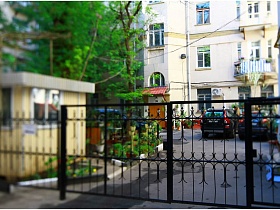 небольшой желтый домик с окнами на придомовой территории двора на Долгоруковской с зеленым полисадником за высоким черным металлическим забором