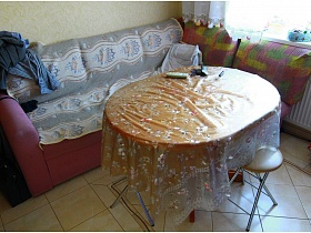 круглые стульчики под обеденным столом с клеенкой у мягкого уголка в кухне трехкомнатной квартиры