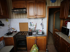 газовая плита с вытяжкой ,железная мойка в шкафу, телевизор на мраморной столешнице коричневой кухни в сталинской квартире