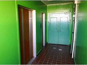 двери лифтов на площадке с зелеными стенами и плиткой на полу в подъезде панельного дома