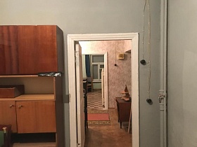 старый деревянный шкаф, открытая проводка с черным выключателем и розеткой на серой стене у открытой двери комнаты с видом на прихожую и  кухню квартиры на Остоженке