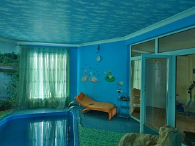 лежак и сервировочый столик у стены с красочным оформлением в голубой комнате с бассейном дизайнерской дачи в сосновом лесу