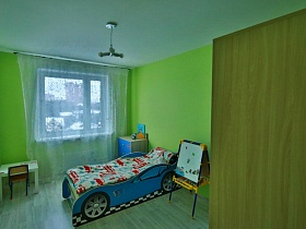 кровать, стилизованная под машину, стульчик у белого столика,планшет в детской комнате с салатневыми стенами молодежной евро квартиры в Новострое