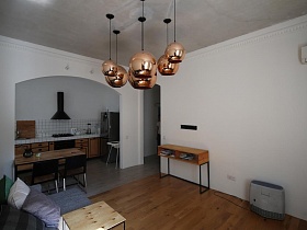 большие кремовые, перламутровые сферические плафоны подвесных светильников на белом потолке светлой гостиной с деревянным обеденным столом на границе разграничения зонированной комнаты скандинавской квартиры