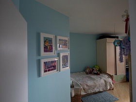 бежевый шкаф для одежды у деревянной кровати с мягкими игрушками на покрывале,яркие картины на голубой стене детской комнаты красивой трехкомнатной квартиры