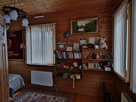 деревянные полочки с книгами, игрушками, грамоты, картина на стене между окнами с жалюзи в спальне загородной дачи
