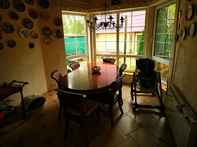 сервировочный столик на колесах, домик для животного, детское кресло и овальный коричневый  стол со стулями у большого полукруглого окна столовой семейной классической дачи