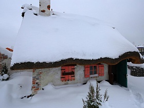 розовые ставни на окнах небольшого дома-мазанки с шапкой снега на крыше на территории ресторана, стилизованного под хутор