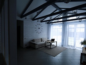 общий вид светлой гостиной с мягким диваном, журнальным столиком и часами на белой стене с зоны кухни загородной дачки