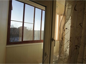 прозрачная гардина с вензелями на окне спальни с выходом на застекленный балкон просторной двухкомнатной квартиры