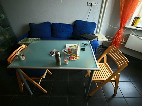 складные деревянные стулья со спинкой вокруг прямоугольного голубого стеклянного стола у синего мягкого дивана на кухне современной семейной квартиры