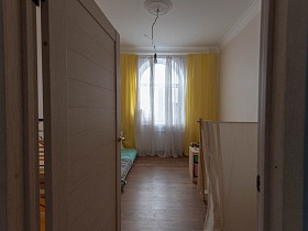 желтые яркие шторы, белая гардина на арочном окне светлой детской через открытую дверь из голубой прихожей