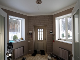 секции отопительных радиаторов на стене под большими окнами, обувь на полу из мозаичной бежевой плитки в прихожей с видеодомофоном у входной двери