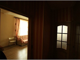 бежевый стул со спинкой у бежевого мягкого дивана с клетчатым покрывалом в светлой гостиной с цветными шторами на большом окне современной двухкомнатной квартиры