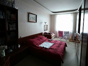 картина наж деревянной кроватью с вишневым покрывалом в спальной комнате семейной трешки