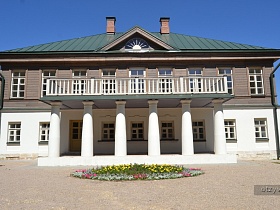 красивое уникальное двухцветное здание двухэтажной школы-музея 19 века с большой цветочной клумбой у крыльца с круглыми колоннами