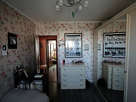 белый шкаф-купе с зеркальными дверцами, белый комод и белые плафоны подвесной люстры в светлой спальне квартиры оператора
