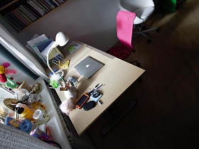 белая настольная лампа, ноутбук,телефон, подставка для книг на поверхности письменного стола с розовыс стулом у окна детской комнаты стильной трешки