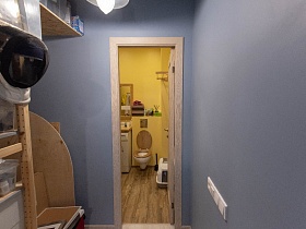 шлем на этажерке с корзинами на полках в голубой прихожей с открытой дверью в ванную комнату с желтыми стенами современной квартиры в разных тонах