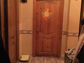 радужное солнышко на деревянной двери в спальную комнату из прихожей с бежевыми обоями на стенах и коричневым линолеумом на полу двухкомнатной квартиры
