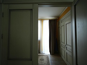 темные шторы и белая гардина на окне с балконной дверью, белый встроенный шкаф для одежды в спальной комнате из открытой межкомнатной двери девчачьей дизайнерской квартиры