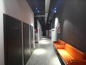 черные и белые стены в длинном коридоре спорт комплекса с ораньжевыми мягкими диванами у стены