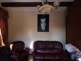 красно-коричневая кожаная мягкая мебель у бежевой стены кабинета с черно-белой картиной