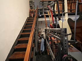 металлическая лестница с деревянными ступенями и перилами на второй этаж музыкального магазина с рядами футляр для гитар