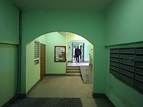 почтовые ящики на стене, арочные переходы к лестнице с пандусом в коридор с лифтами в зеленом подъезде многоэтажного дома