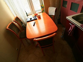 рыжий обеденный стол и стулья со спинками в кухне с бежевыми стенами в семейной трешке
