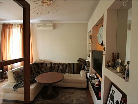 открытые двери в светлую гостиную с бежевым мягким диваном и круглым столиком на ковре в семейной трехкомнатной квартире
