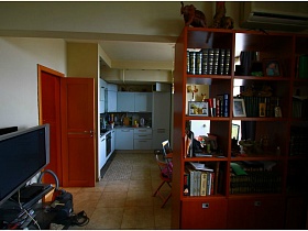 телевизор на тумбе, книги на открытых полках книжного шкафа в зонированной комнате двухкомнатной квартиры с видом на Москва-сити