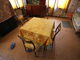стулья со спинкой и желтыми чехлами  вокруг квадратного стола с желтой скатертью с бахромой посередине гостиной на даче времен СССР