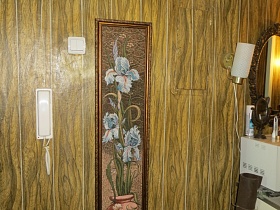 декоративное пано в рамке рядом с белым выключателем, белым телефоном и бра на стене под дерево в прихожей квартиры молодой советской семьи