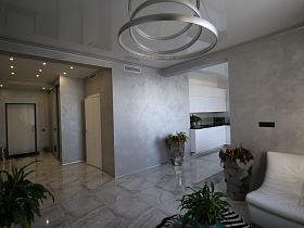 открытые дверные проемы из гостиной в просторный коридор и кухню с белой мебелью современной квартиры в лаконичном сером хай-тек исполнении