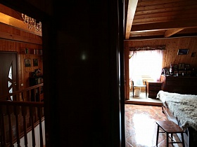 спальная комната с деревянной кроватью, комодами с фотографиями, большим окном под деревянной крышей семейной классической дачи