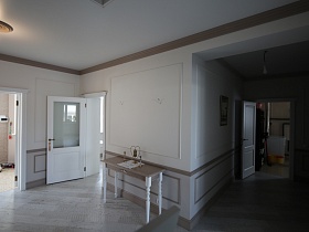 открытые белые двери в прихожую, на кухню и хозяйственную комнату з просторного светлого вестибюля с лестницей на второй этаж загородного дома