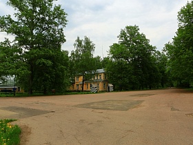 просторная асфальтированная площадка в окружении высоких зеленых деревьев, желтых ярких деревянных домов в старом городке