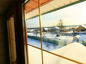 вид на огромный сугроб снега во дворе у забора и соседние дома из окна деревянного дома на открытой террасе