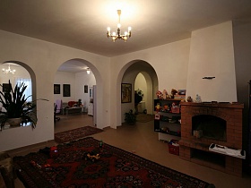 кирпичный камин в просторной гостиной с кремовыми стенами и арочными переходами в разные комнаты гостевого двухэтажного дома с придорожным кафе