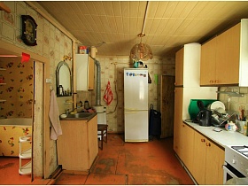 ванна за стенкой просторной кухни с бежевой мебелью и белым холодильником у стены
