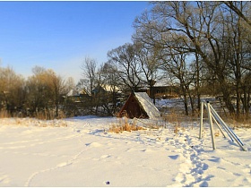 протоптанная дорожка в снегу к колодцу с водой под треугольной крышей на поляне в окружении деревьев и кустарников