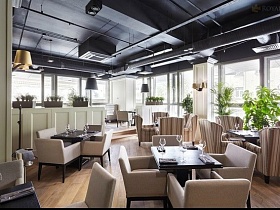 белые и полосатые кресла у столиков под черным потолком ресторана в центре Москвы