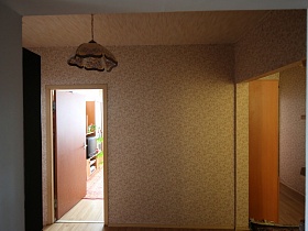 просторный холл с бежевыми обоями на стенах и потолке со стеклянным бежево-коричневым плафоном подвесной люстры современной типичной квартиры