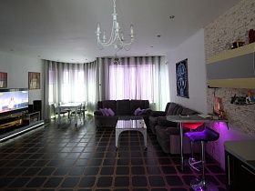 большая просторная светлая гостиная с серым мягким гарнитуром,журнальным столикои и телевизором у стены креативного дома
